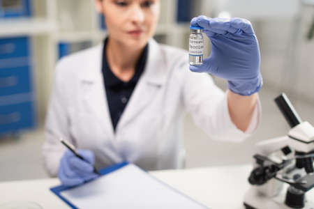 blurred doctor in latex gloves holding coronavirus vaccine in clinic