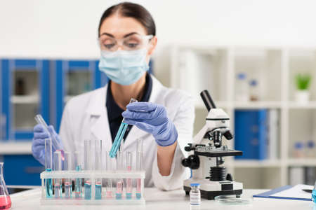 Test tubes near microscope and blurred scientist in laboratory
