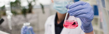 Cropped view of blurred scientist in latex gloves holding flask in laboratory, bannerの写真素材