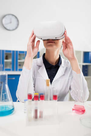 Smiling scientist in virtual reality headset near blurred test tubes and flasks in labの写真素材