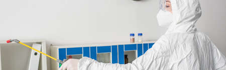 doctor in goggles and hazmat suit making disinfection of laboratory with sprayer, bannerの写真素材