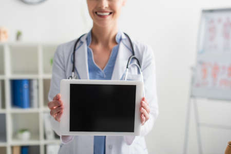 Cropped view of digital tablet with blank screen in hands of smiling doctor in hospitalの写真素材