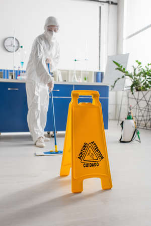 attention board near doctor in hazmat suit cleaning floor with mopの写真素材