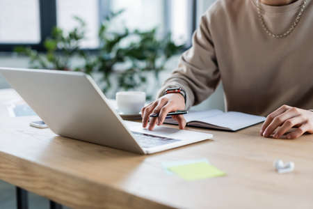 Cropped view of businessman using laptop near notebook and coffee in officeの写真素材