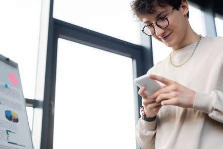 Low angle view of young businessman using mobile phone near flip chart in office