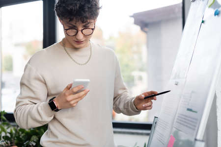 Young businessman using cellphone near flip chart in office