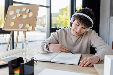 Smiling transgender person in headphones looking at notebook in officeの写真素材