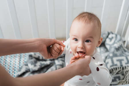 woman holding hands of cheerful little son standing in crib