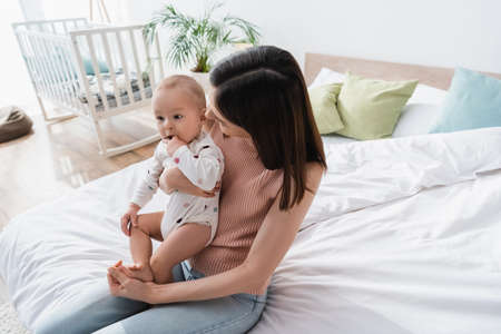 brunette woman sitting with little son on bed at home