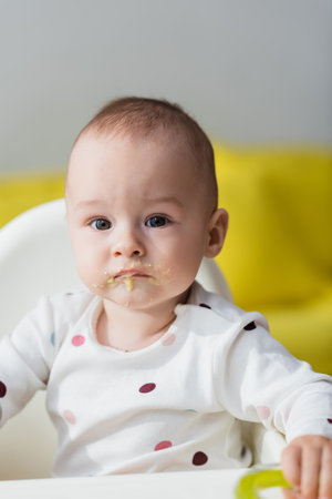 toddler child with food on lips sitting in baby chair