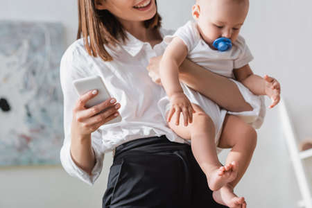 blurred woman holding smartphone and little son in romperの写真素材