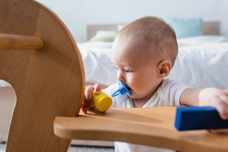 little boy with pacifier holding building blocks near blurred rocking horseの写真素材