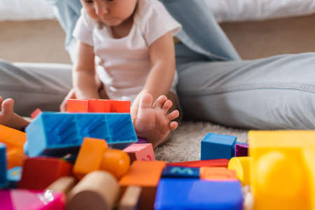 blurred woman and baby boy playing with building blocks on floor at home