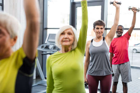 Elderly woman working out with dumbbells near multiethnic friends in gymの写真素材