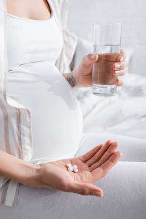 partial view of tattooed pregnant woman holding glass of water and pillsの写真素材