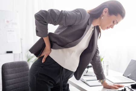 pregnant businesswoman suffering from pain and leaning on desk in officeの写真素材