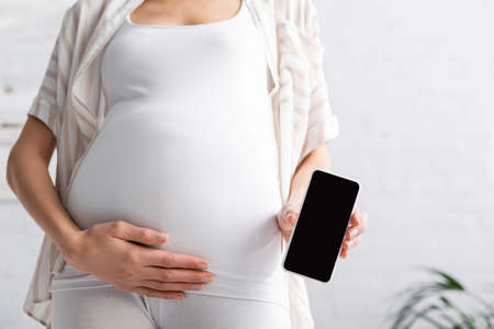 cropped view of pregnant young woman holding smartphone with blank screenの写真素材