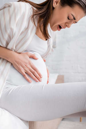 young pregnant woman with closed eyes suffering from cramp