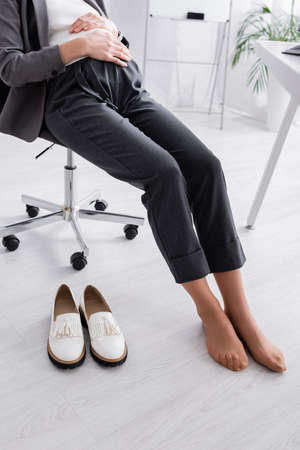 cropped view of shoeless pregnant woman sitting on chair near deskの写真素材