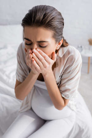 young pregnant woman feeling nausea and covering mouthの写真素材
