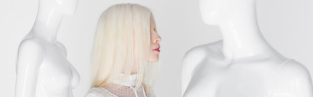 Side view of albino woman standing between mannequins isolated on white, bannerの写真素材
