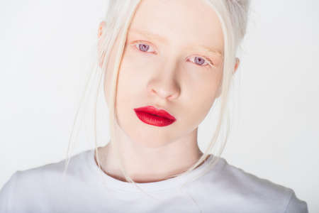 Portrait of albino woman with red lips in white t-shirt looking at camera isolated on whiteの写真素材