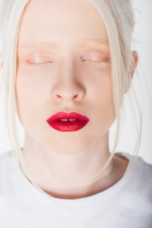 Portrait of young albino woman with red lips closing eyes isolated on whiteの写真素材