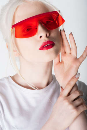 Portrait of albino model in red sunglasses touching face isolated on whiteの写真素材