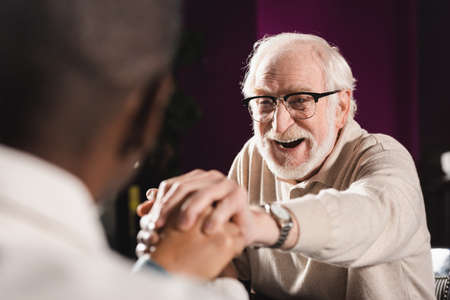 cheerful senior man holding hands of blurred african american man during meeting in pubの写真素材