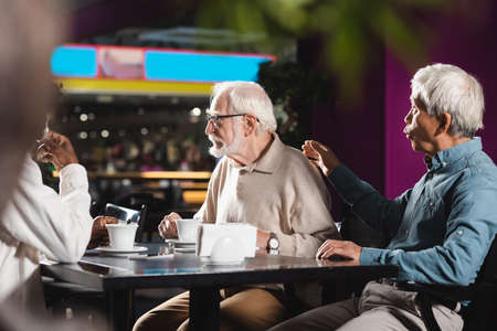 asian man touching back of senior friend near blurred african american man in cafeの写真素材