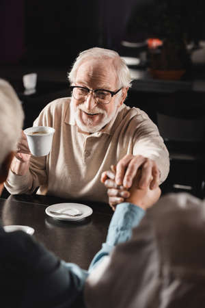 cheerful senior man joining hands with blurred interracial friends in cafeの写真素材