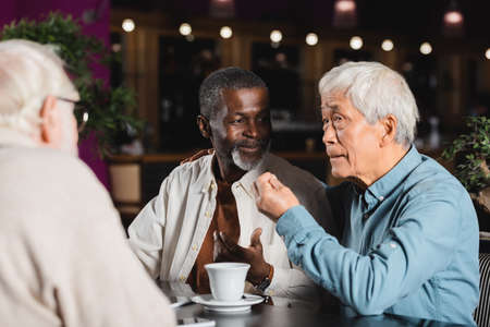 senior asian man gesturing while talking to multicultural friends in restaurantの写真素材