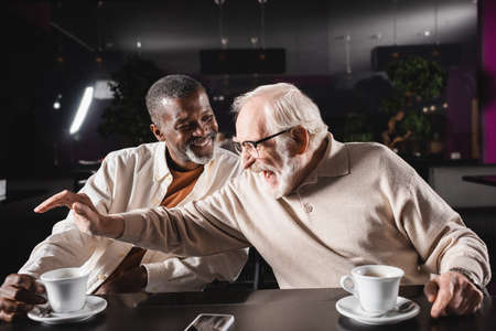 excited senior man gesturing near happy african american man in cafeの写真素材