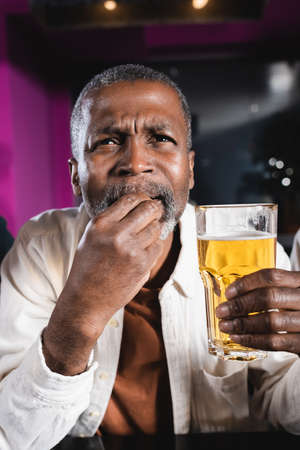 senior african american man holding glass of beer while watching championship in sports barの写真素材