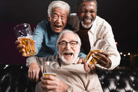 elderly friends with glasses of beer laughing at camera in pubの写真素材