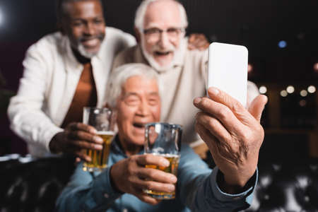 blurred asian man taking selfie on mobile phone with senior friends in beer pubの写真素材