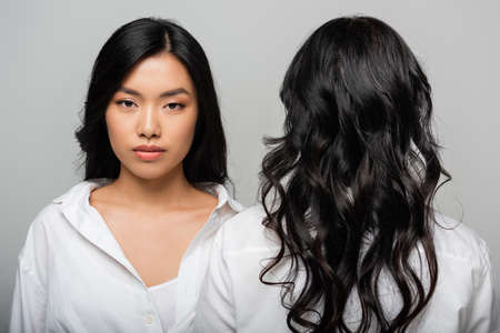 back view of brunette asian mother near young adult daughter isolated on greyの写真素材