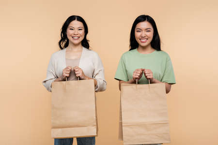 happy asian mother and daughter with paper bags isolated on beigeの写真素材