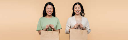 happy asian mother and daughter with shopping bags isolated on beige, bannerの写真素材