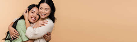 cheerful asian mother and daughter hugging isolated on beige, bannerの写真素材