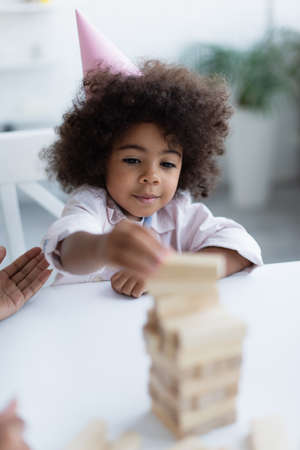 curly african american child in party cap playing wood blocks game on blurred foregroundの写真素材