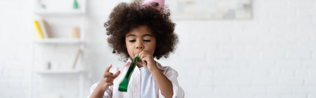 curly african american child blowing in party horn, bannerの写真素材