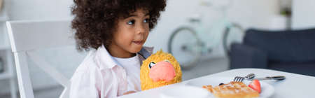 african american girl with soft toy sitting at table near waffle on plate, bannerの写真素材