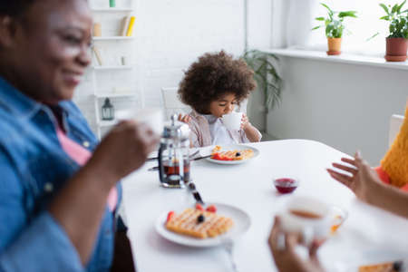 african american child drinking tea during breakfast with blurred granny and momの写真素材