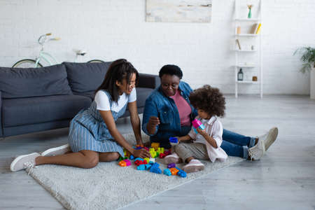 african american women playing building blocks game with toddler girl on floor at homeの写真素材