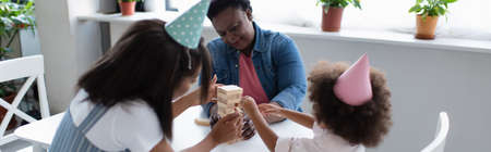 african american women and toddler child in party caps playing wood blocks game at home, bannerの写真素材