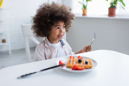 african american kid holding fork near tasty waffle with fresh berries on plateの写真素材