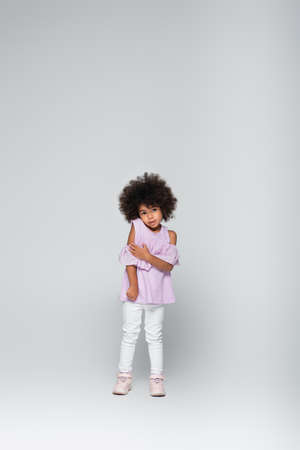 full length view of african american kid in violet blouse and white pants standing on greyの写真素材