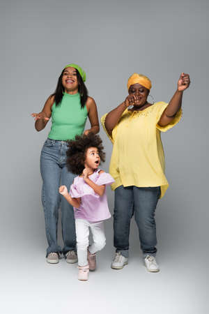 african american girl dancing with mother and granny in stylish clothes on greyの写真素材