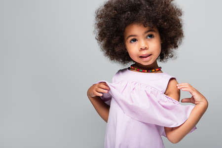 curly african american girl in violet blouse and colorful beads posing isolated on greyの写真素材